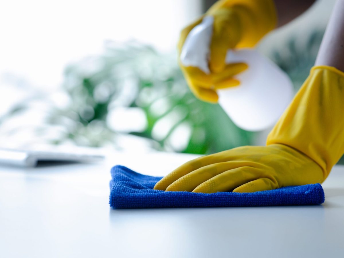 Person cleaning the room, cleaning staff is using cloth and spraying disinfectant to wipe the tables in the company office room. Cleaning staff. Maintaining cleanliness in the organization.