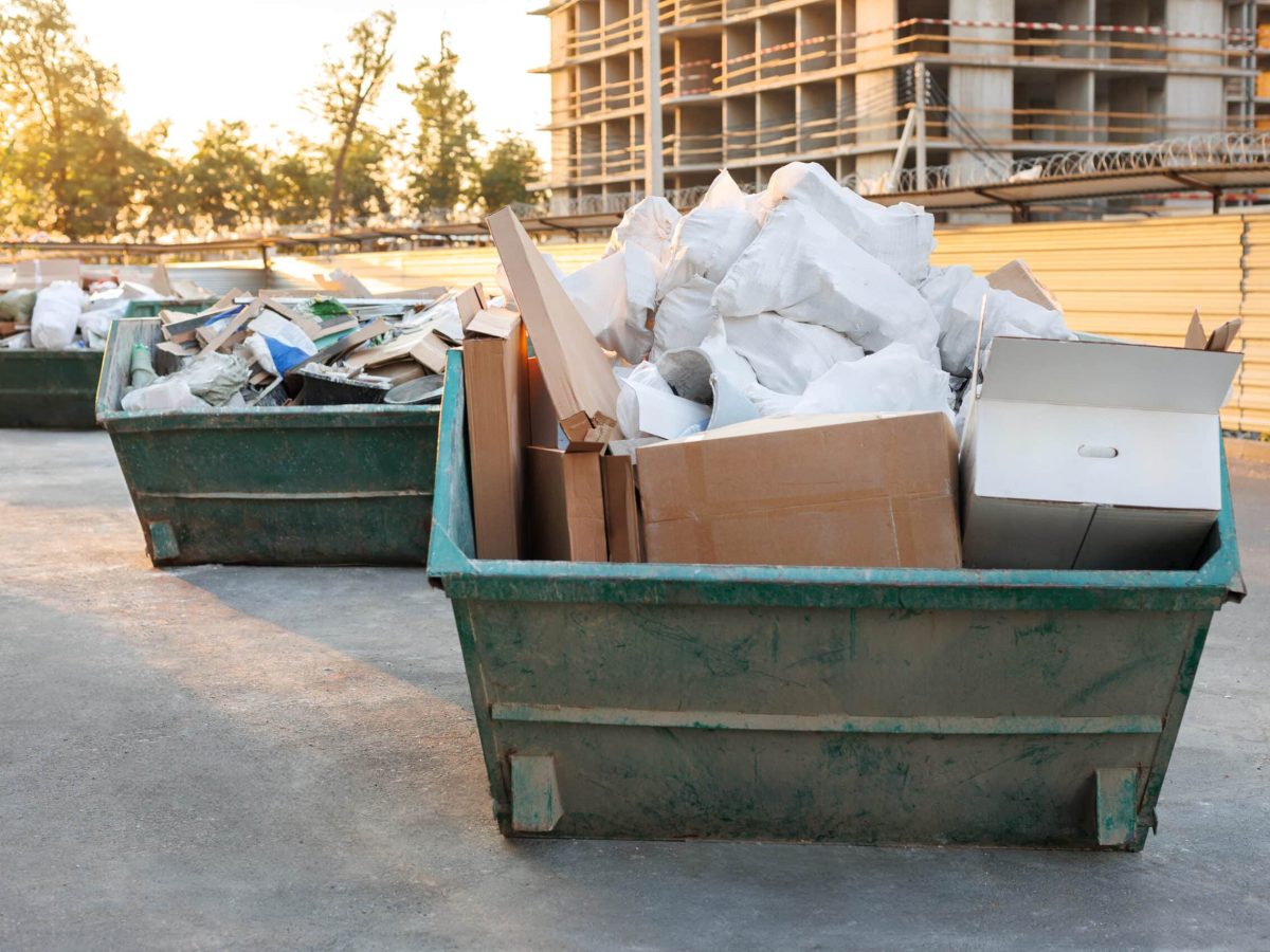 Garbage cans stand next to a house under construction at sunset. Container with construction debris