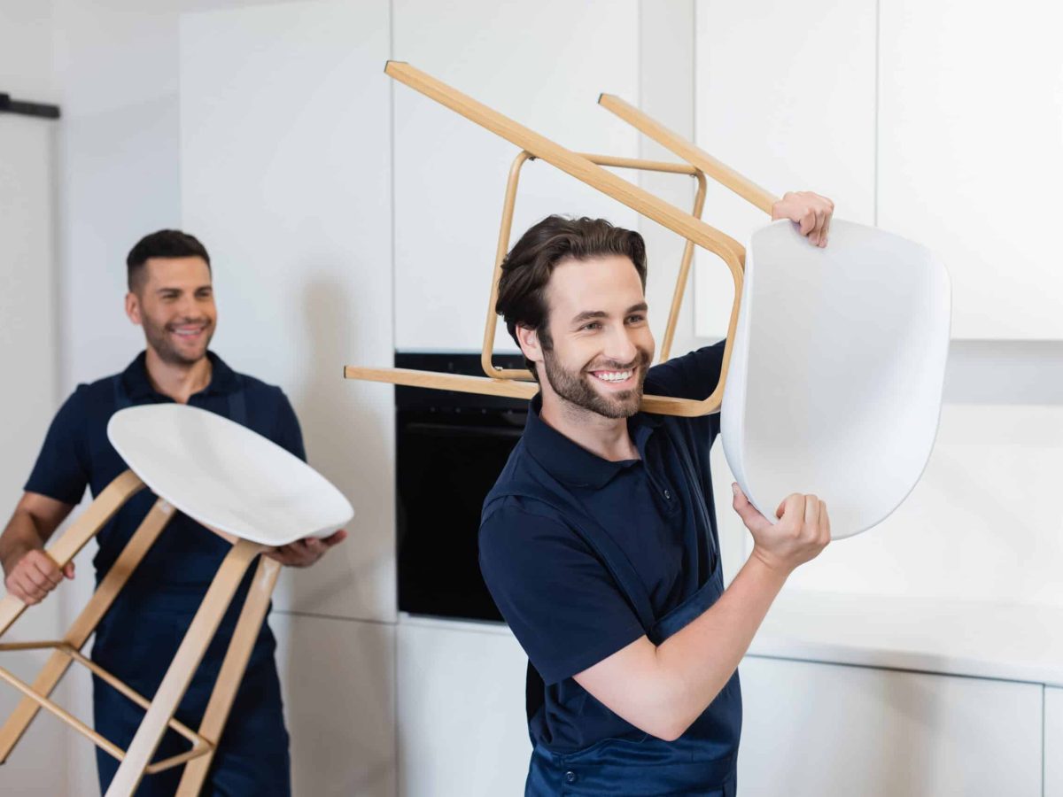 smiling movers carrying white stools in kitchen